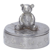 Silver teddy bear on top of a round silver box with paw print design on a white background